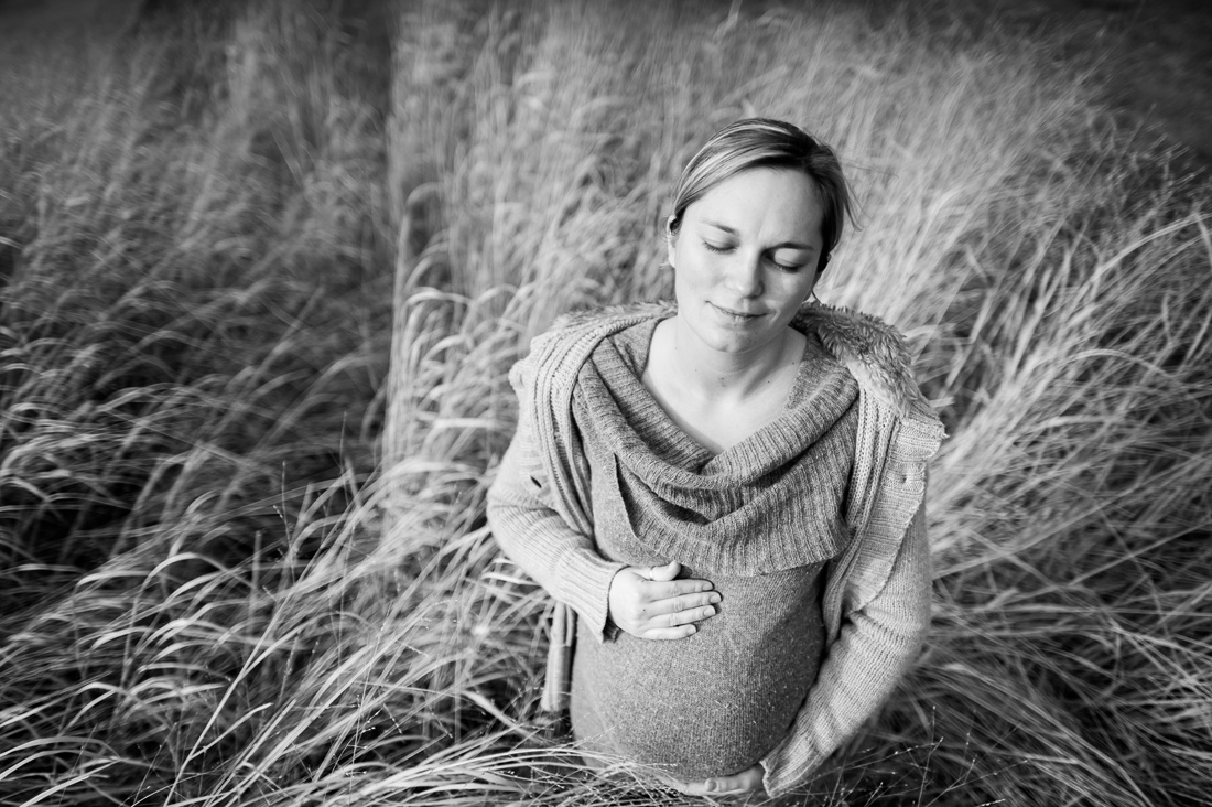 vue par en plongée d'une femme enceinte qui ferme les yeux en se tenant le ventre. Elle est dans de grandes herbes. Photographie Noir et blanche.