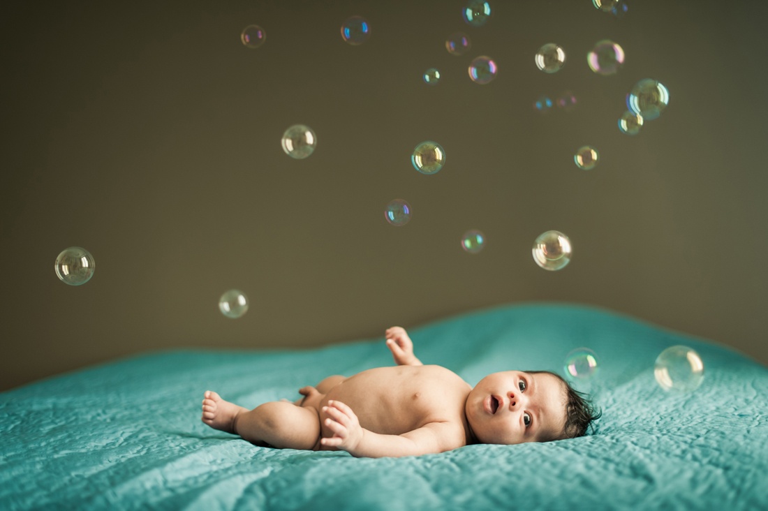 Un bébé nu sur un lit il regarde les bulles de savon tomber sur lui. Photo couleur originale.