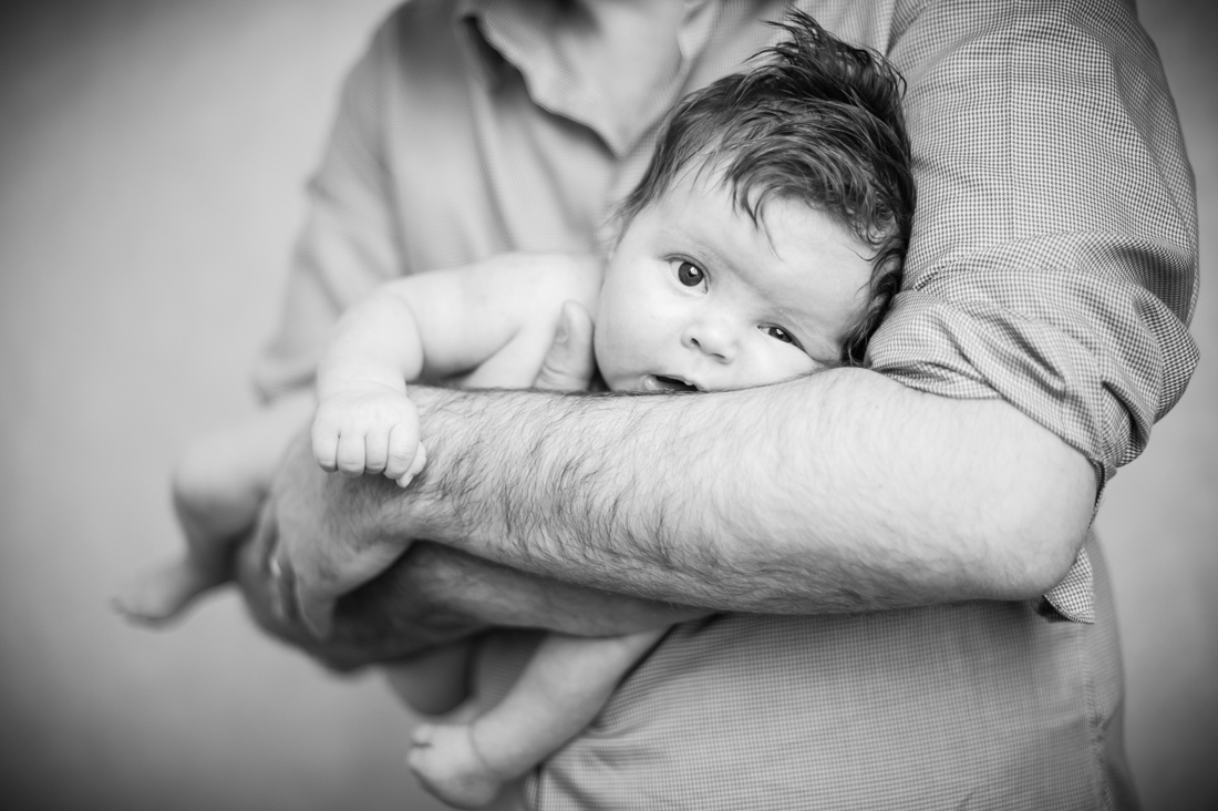 un bébé nouveau né dans les bras de son papa. Photo en noir et blanc.